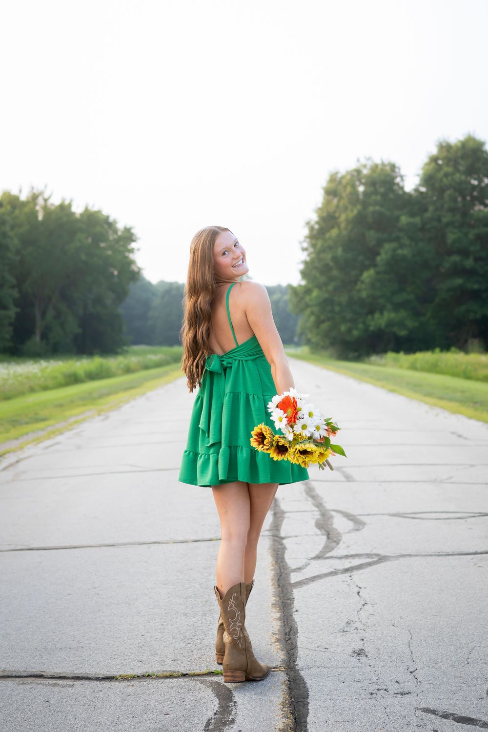 Summer portrait on a rural road featuring a green dress and cowboy boots with wildflowers.