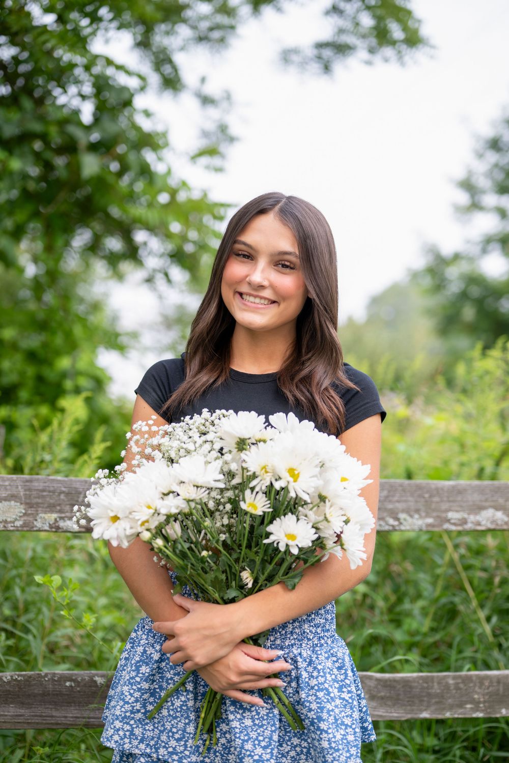 Portrait series with daisy bouquet and blue floral skirt on wooden fence.