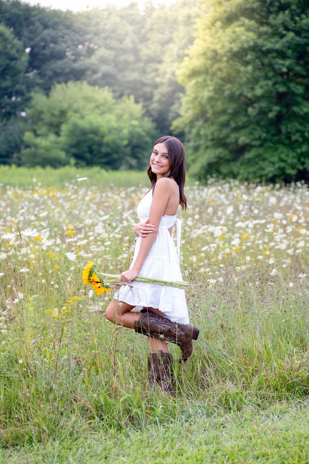 A dreamy summer portrait in a white dress holding sunflowers in a meadow of wildflowers.
