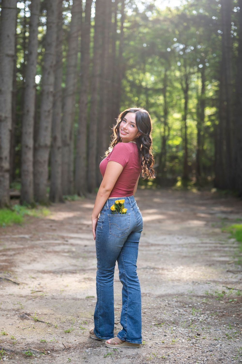 Standing on forest path surrounded by tall pine trees in casual attire.