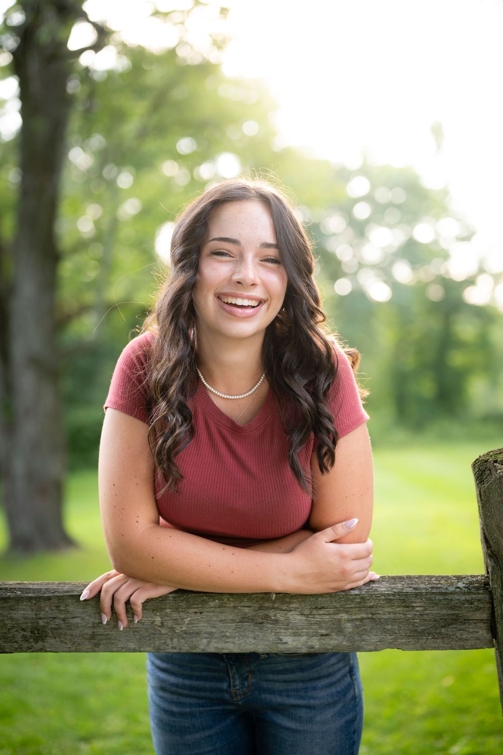 Outdoor portrait leaning on wooden fence in park with warm sunlight and trees in background.
