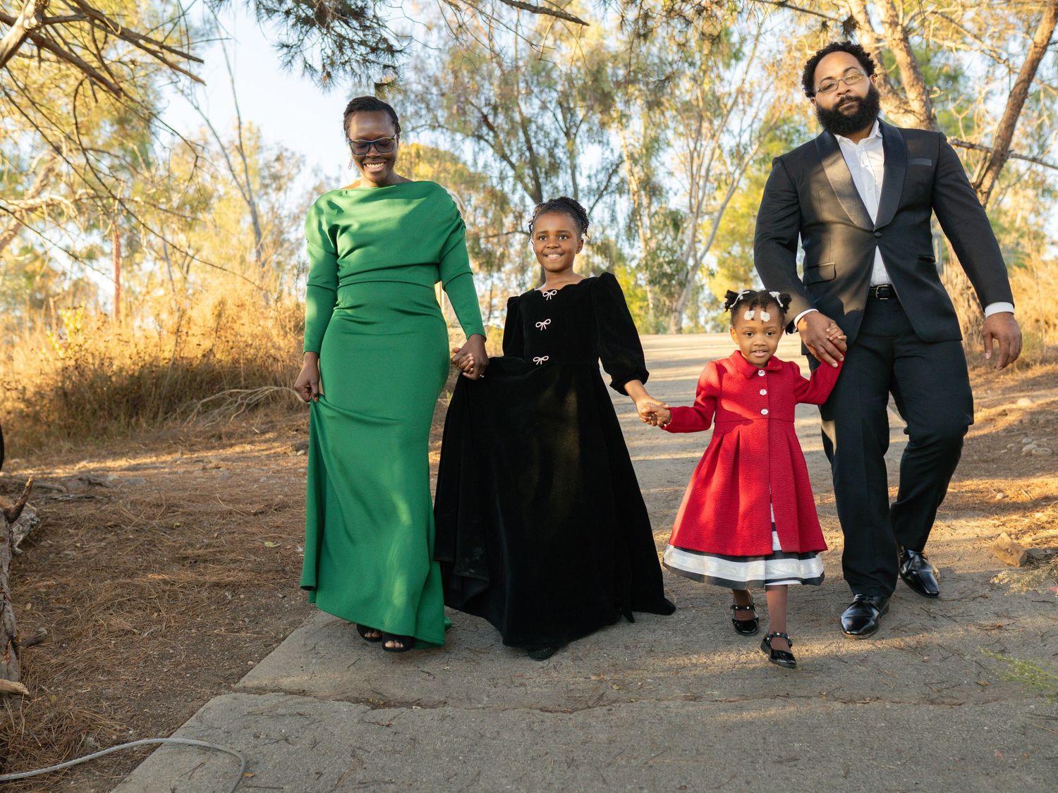 A family walks together on a path, dressed in formal attire including a green gown and red dress.