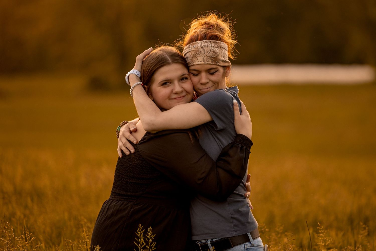 Two people embracing warmly in a golden sunlit field at sunset.