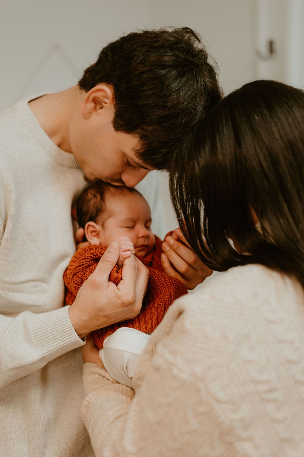 New parents sharing an intimate moment with their newborn baby in warm cream tones.