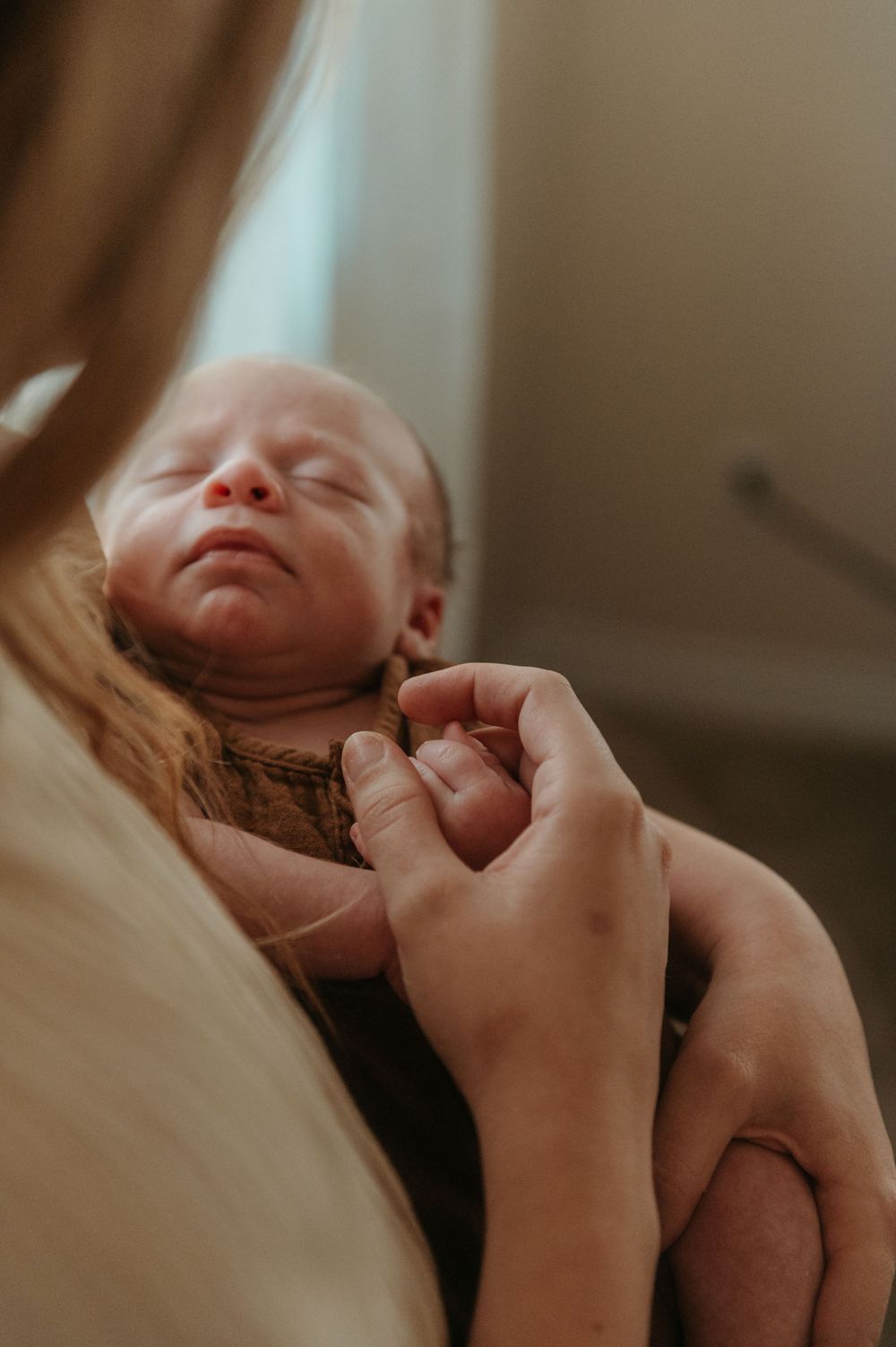 A peaceful newborn baby rests while gentle hands hold them close in warm lighting.
