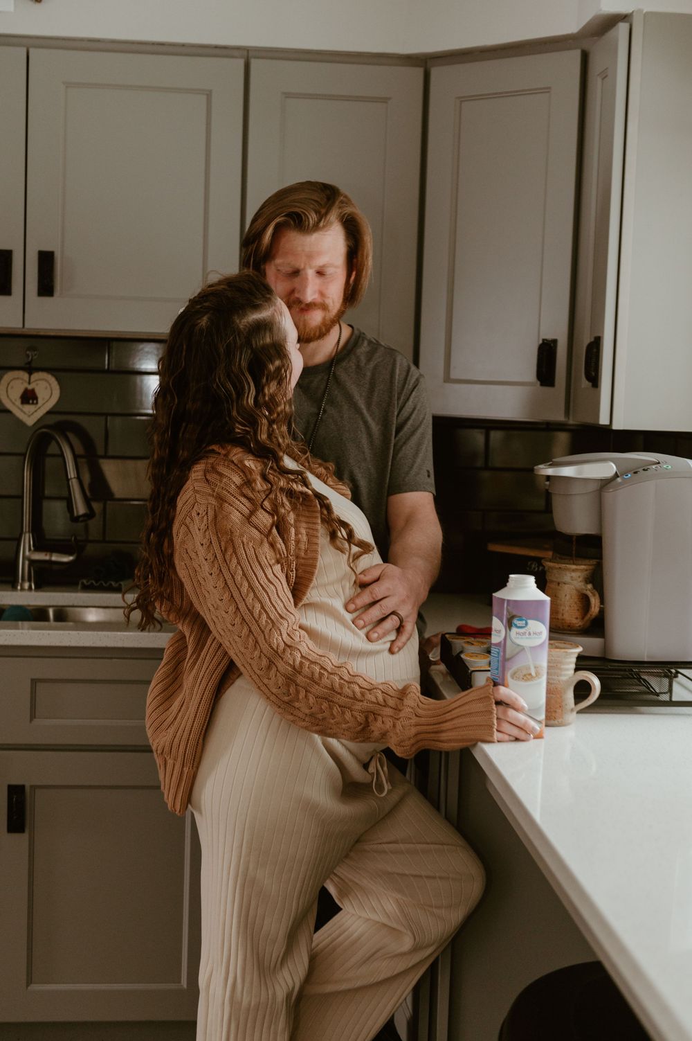 Couple shares intimate moment in cozy kitchen while holding milk carton and wearing warm sweaters.