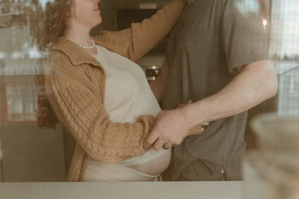 A couple in casual clothing holds each other close while dancing together in a softly lit indoor setting.