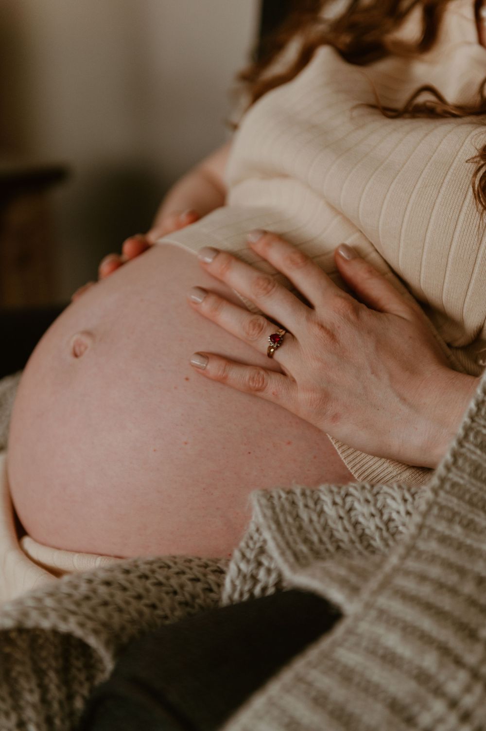 Close up view of hands gently resting on a pregnant belly while wearing a cream ribbed sweater.