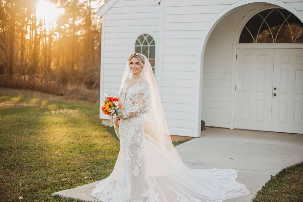 An elegant wedding dress with lace details and long train photographed at sunset in front of a white church.