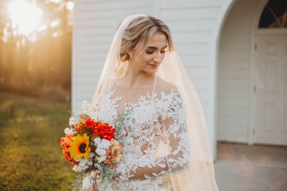 Close-up shot of lace wedding dress details and colorful sunflower bouquet against white church background.