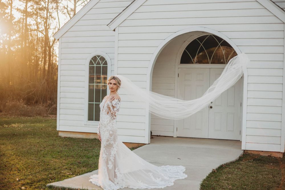 Ethereal bridal portrait showcasing a lace gown with flowing train against white chapel architecture.