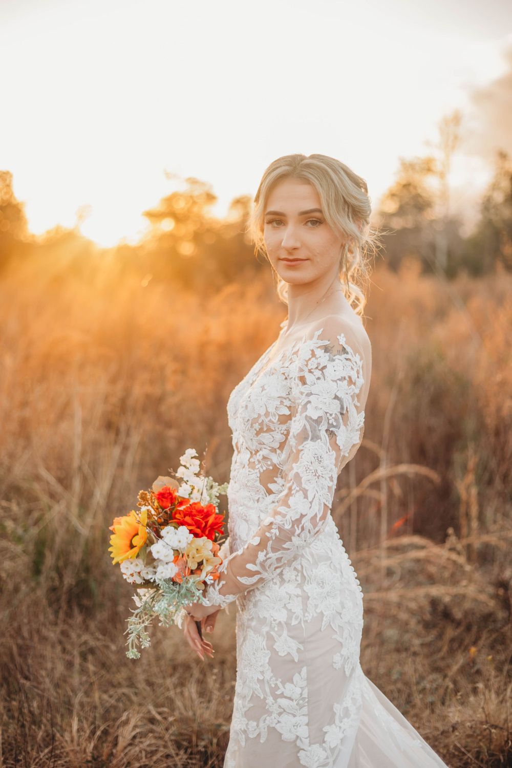Romantic sunset bridal portrait featuring lace dress and autumn-colored bouquet in golden field.
