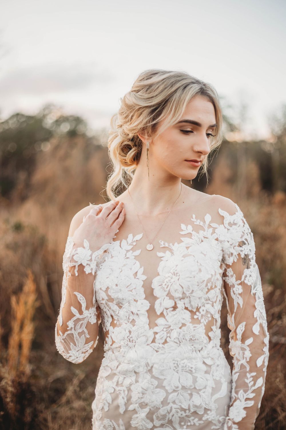 Detailed shot of intricate lace wedding gown with sheer sleeves in warm evening light.