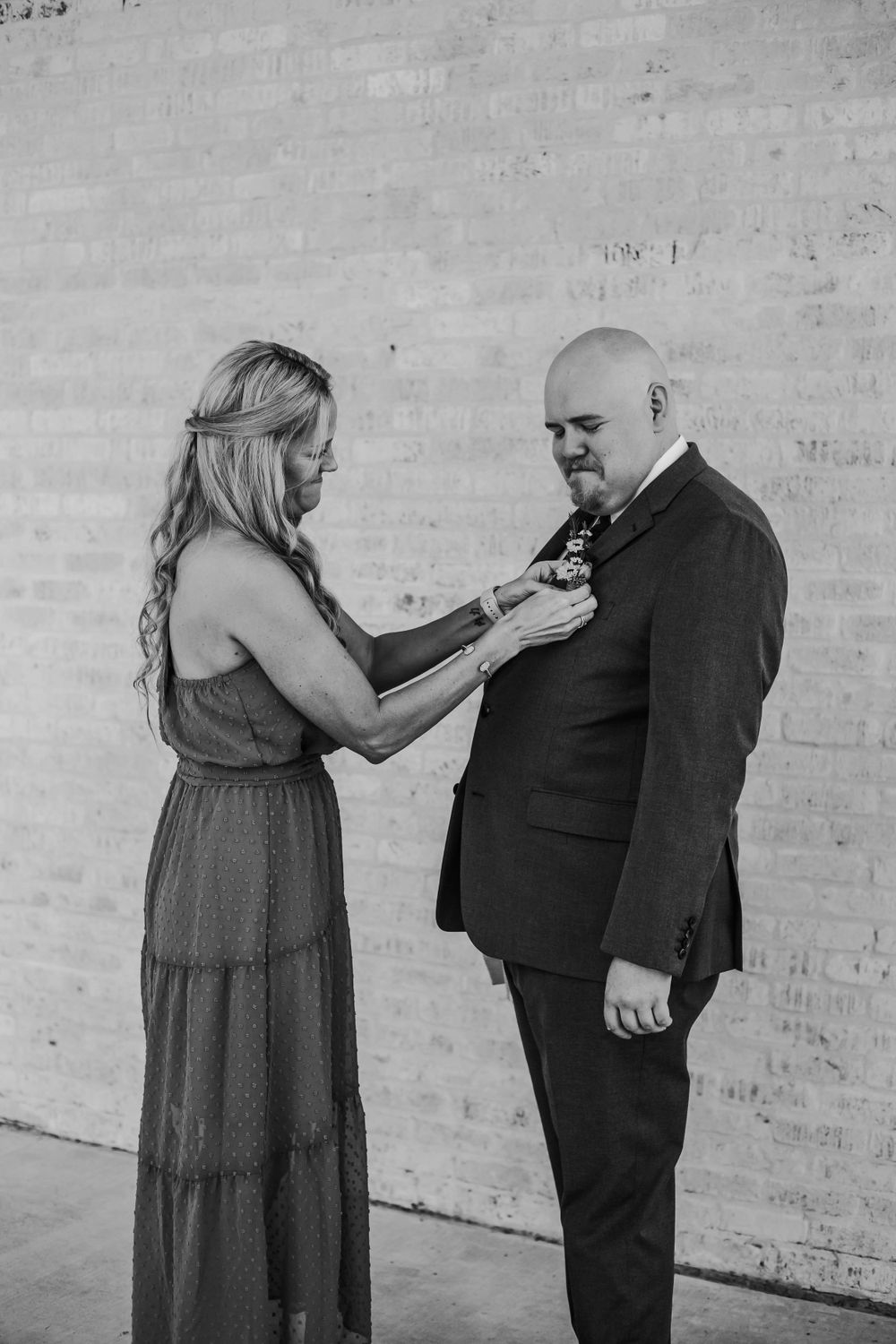 Black and white photograph of formal attire preparation against brick wall background.