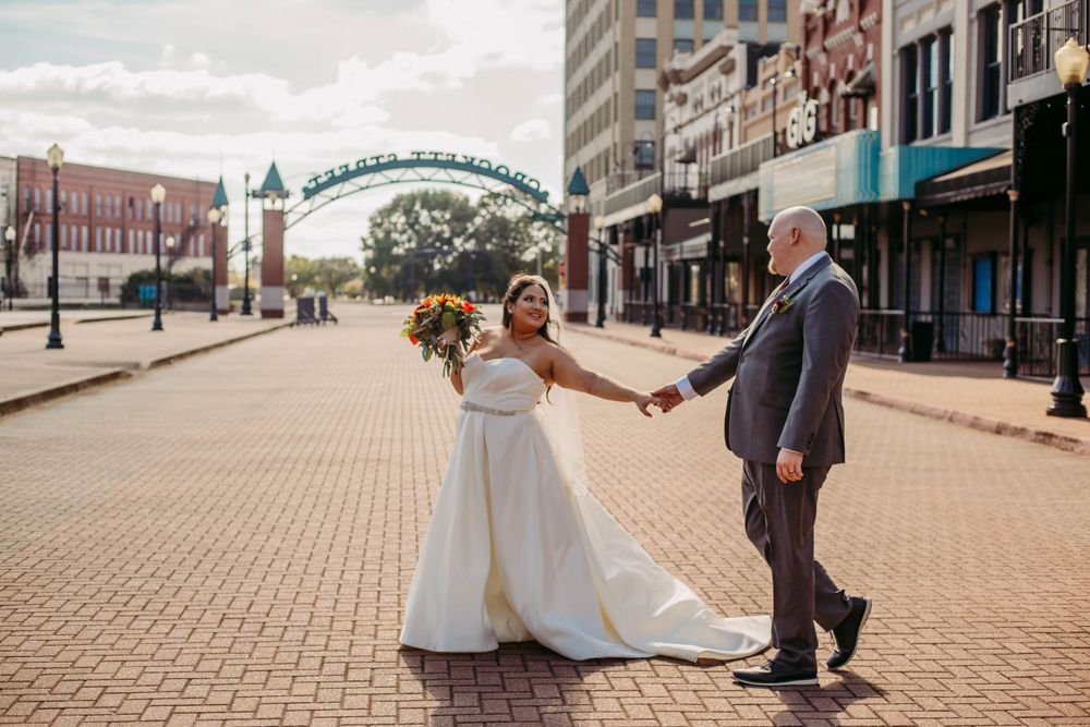 Couple dancing joyfully on brick pavement with decorative arch in background.