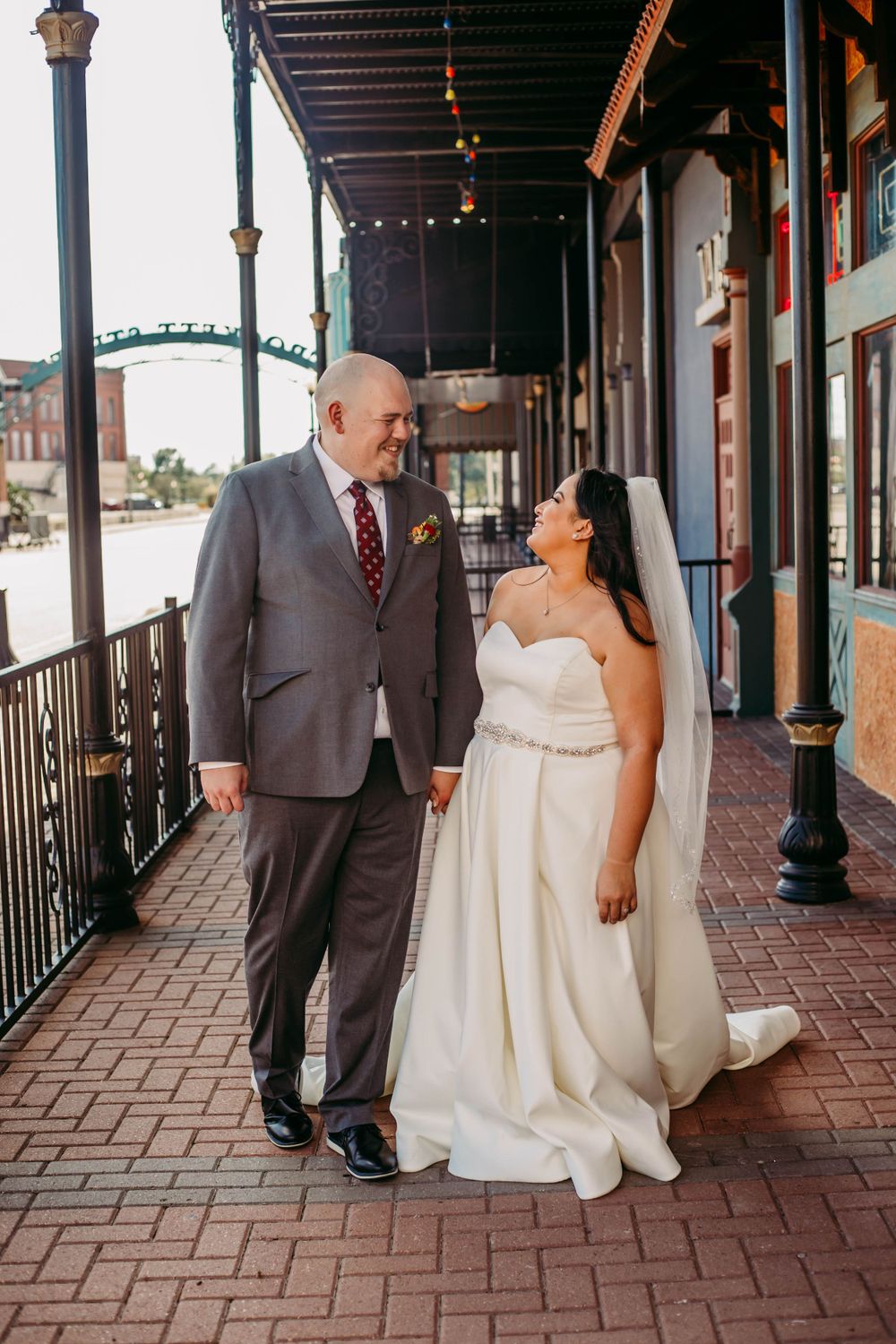 Wedding couple walking together on brick sidewalk under covered storefront.