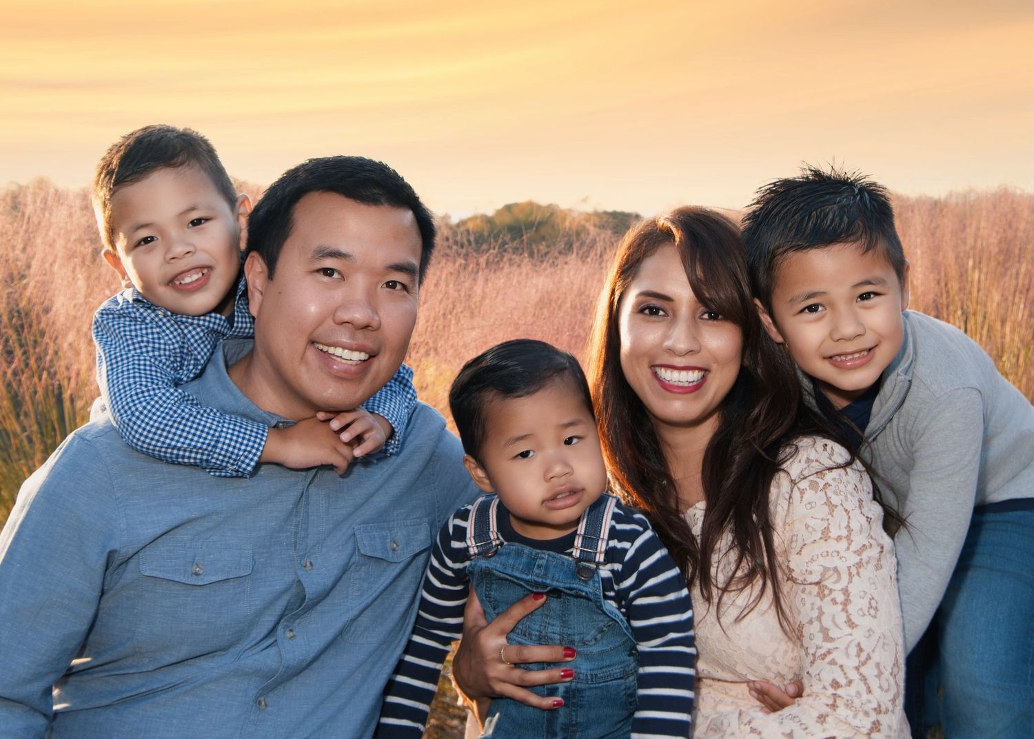 Happy family of five posing together outdoors during golden hour in a field.
