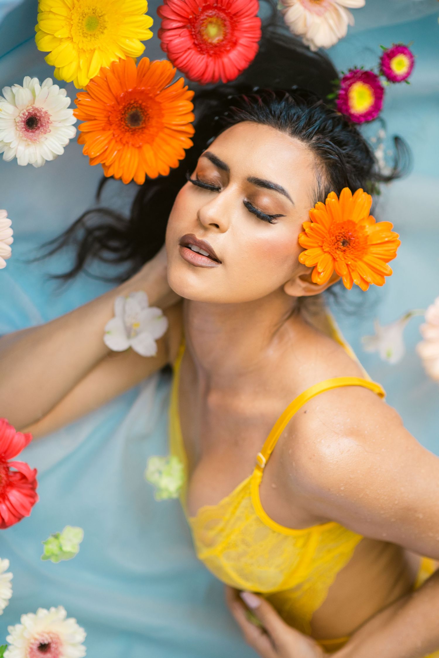 Creative portrait with vibrant orange and red gerbera daisies floating in blue water.