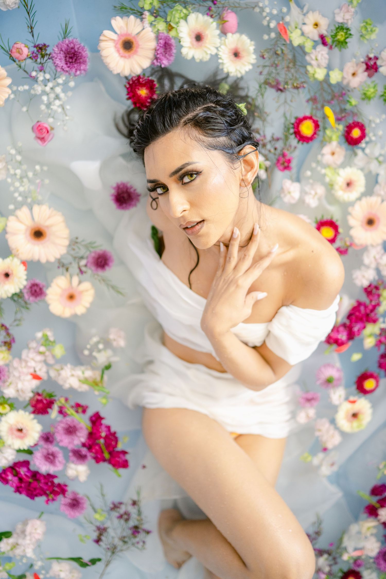 Ethereal milk bath photography with subject surrounded by pink and white flowers.