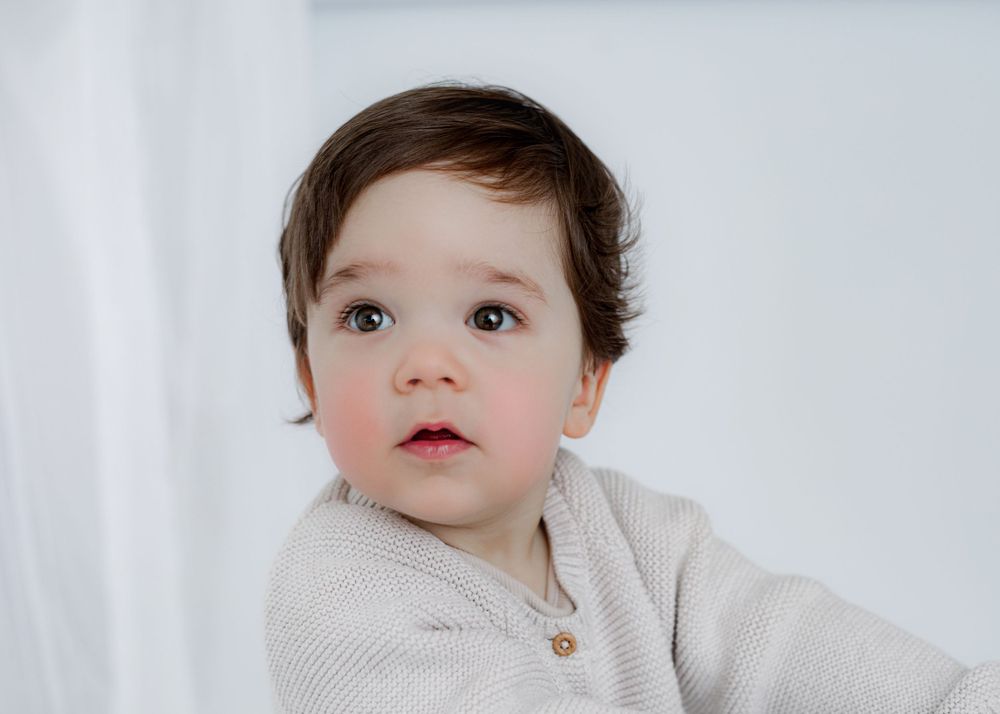 A close-up portrait of a young child in a cream-colored sweater.