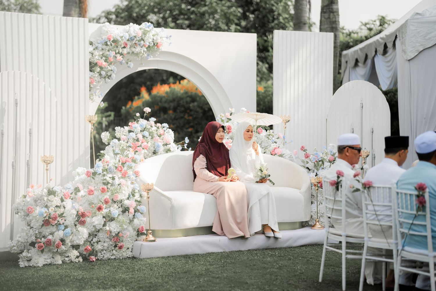 Elegant outdoor wedding seating area with white floral arch and blush pink decor.