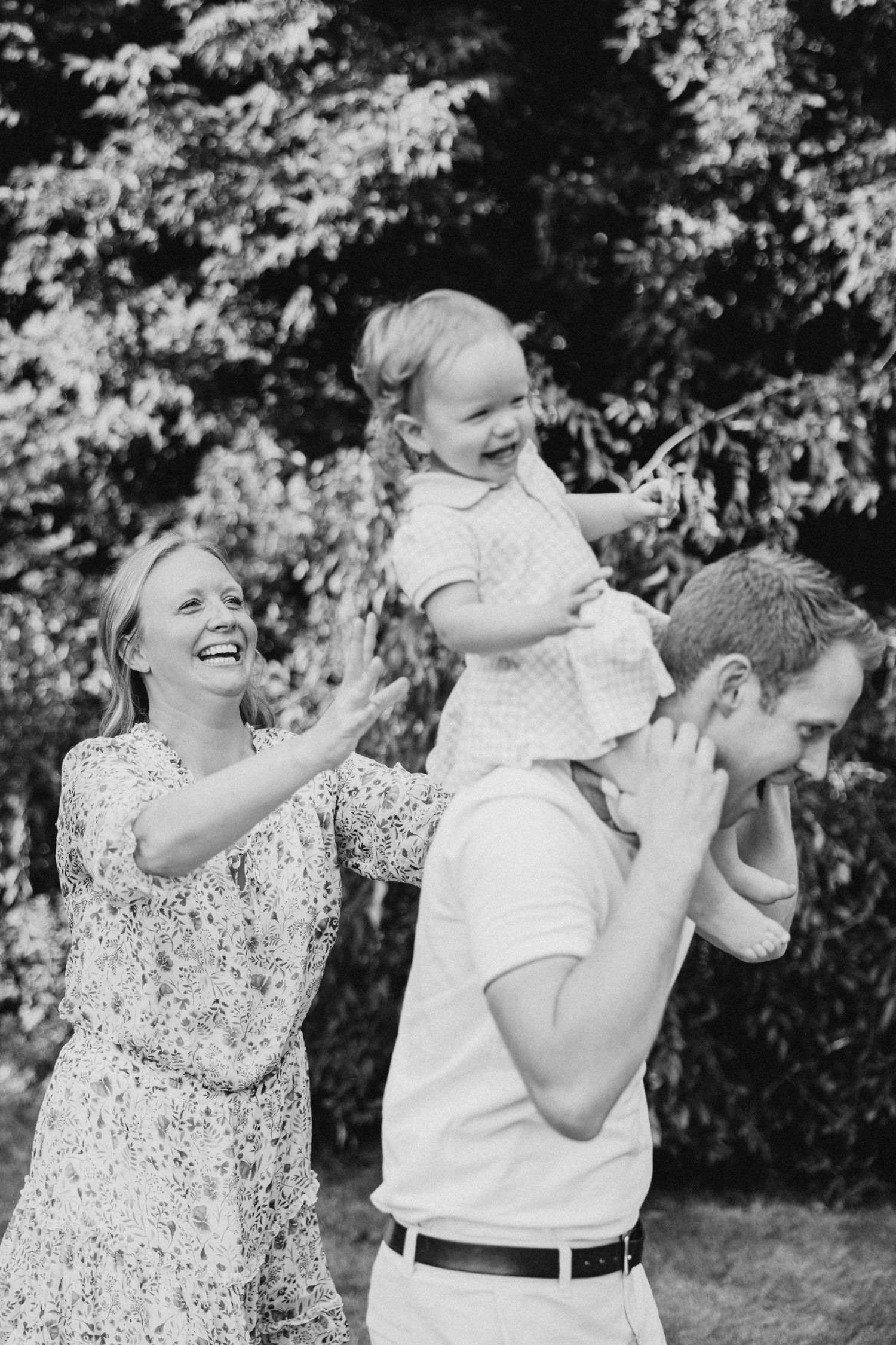 A joyful moment captured in black and white as a family plays and laughs together outdoors in a garden setting.