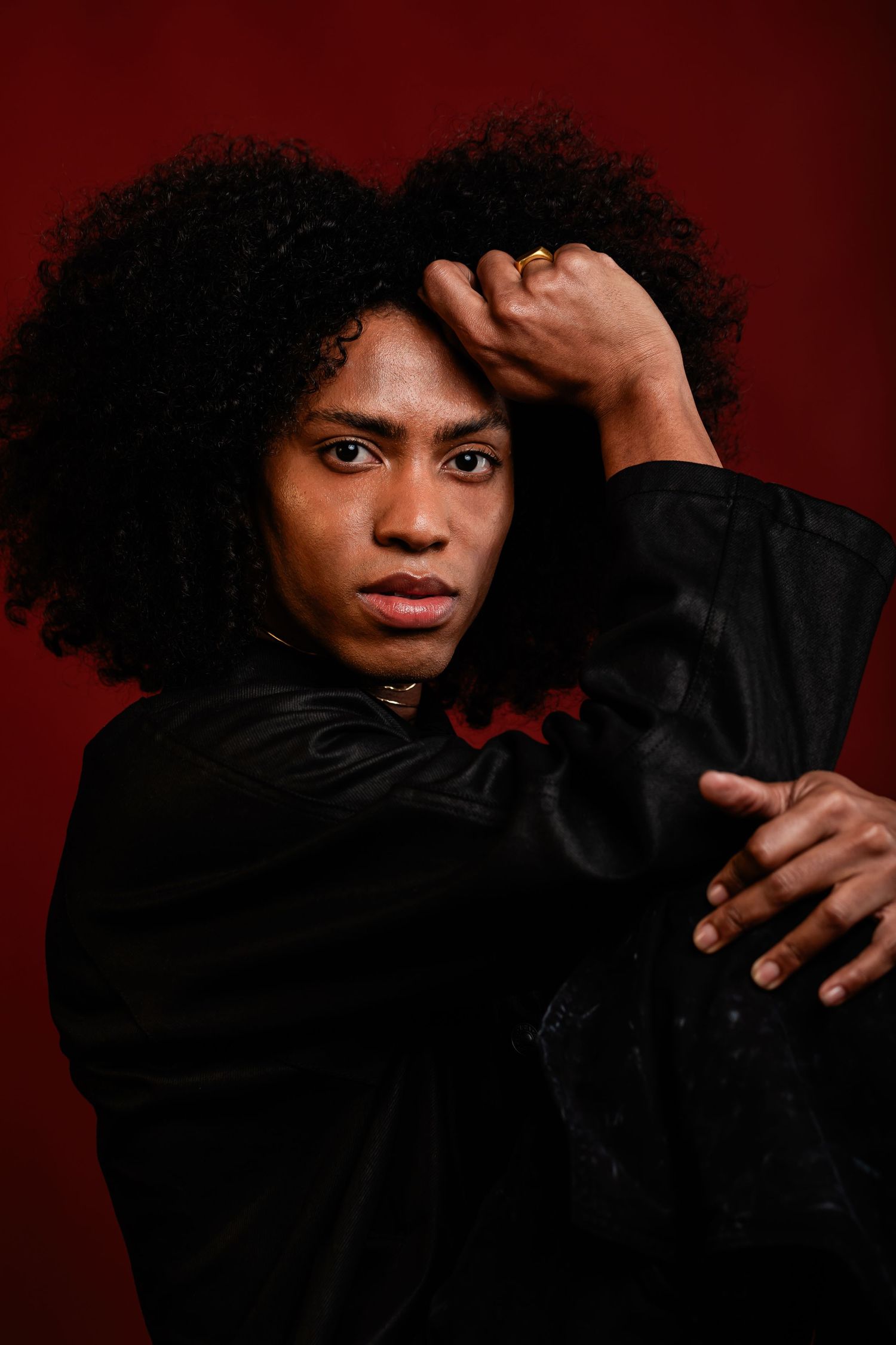 Portrait against dark red background featuring dramatic pose in black attire.