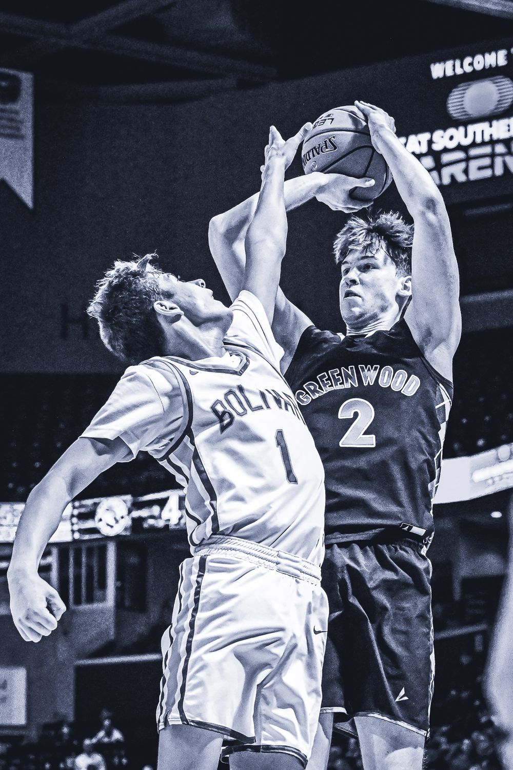 Two basketball players jump for ball during intense game action in black and white photo.