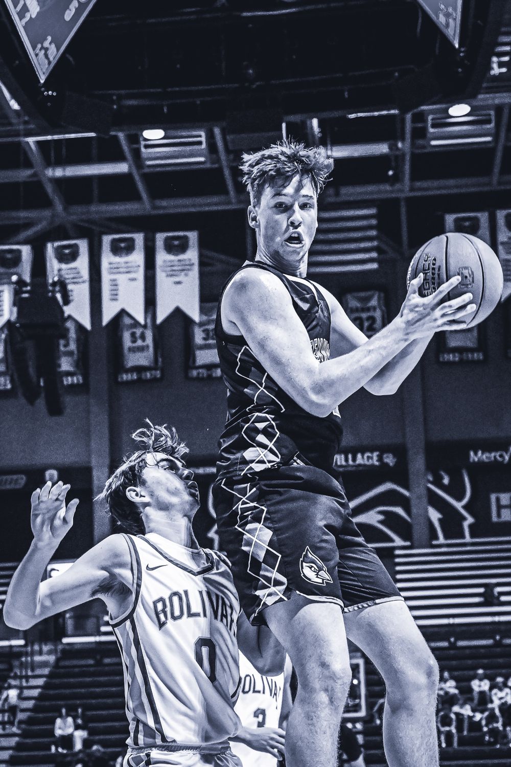 Basketball player leaps for shot while defender attempts block in indoor arena.