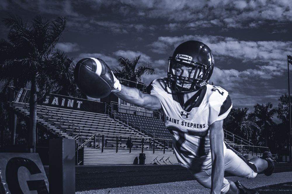 Football player in white uniform dives for catch in monochromatic stadium photo.