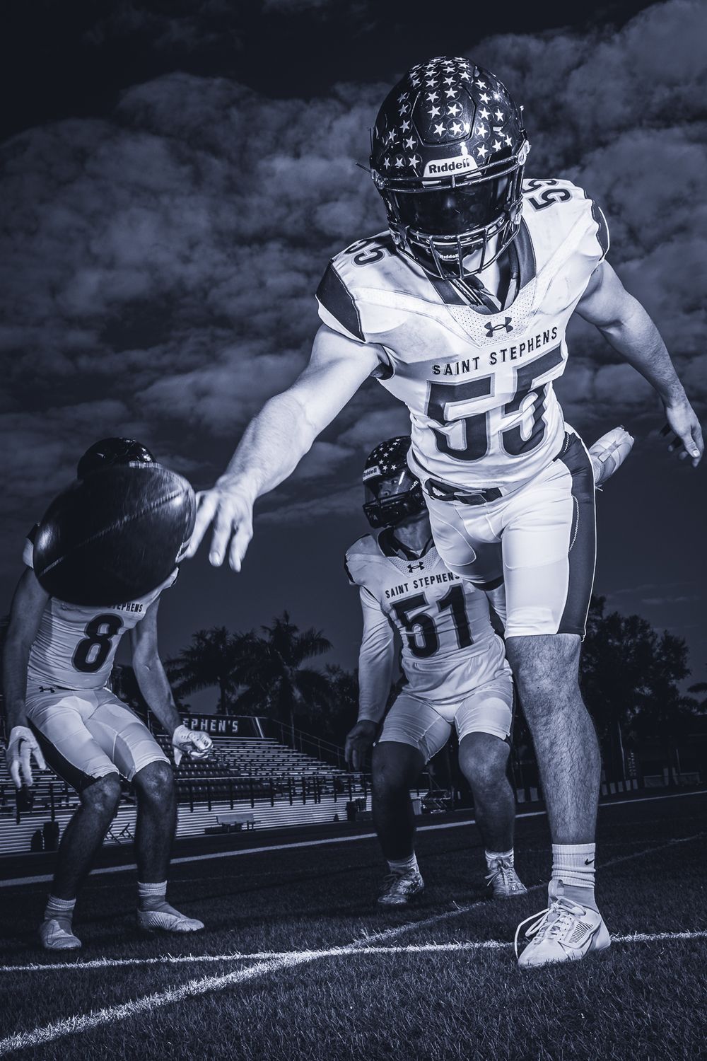 Football players engage in dramatic play during night game in black and white action shot.