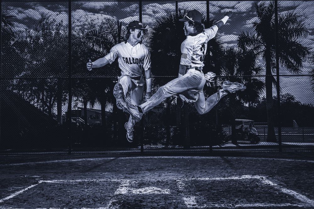 Two athletes jump in synchronized motion on sports field in black and white photo.