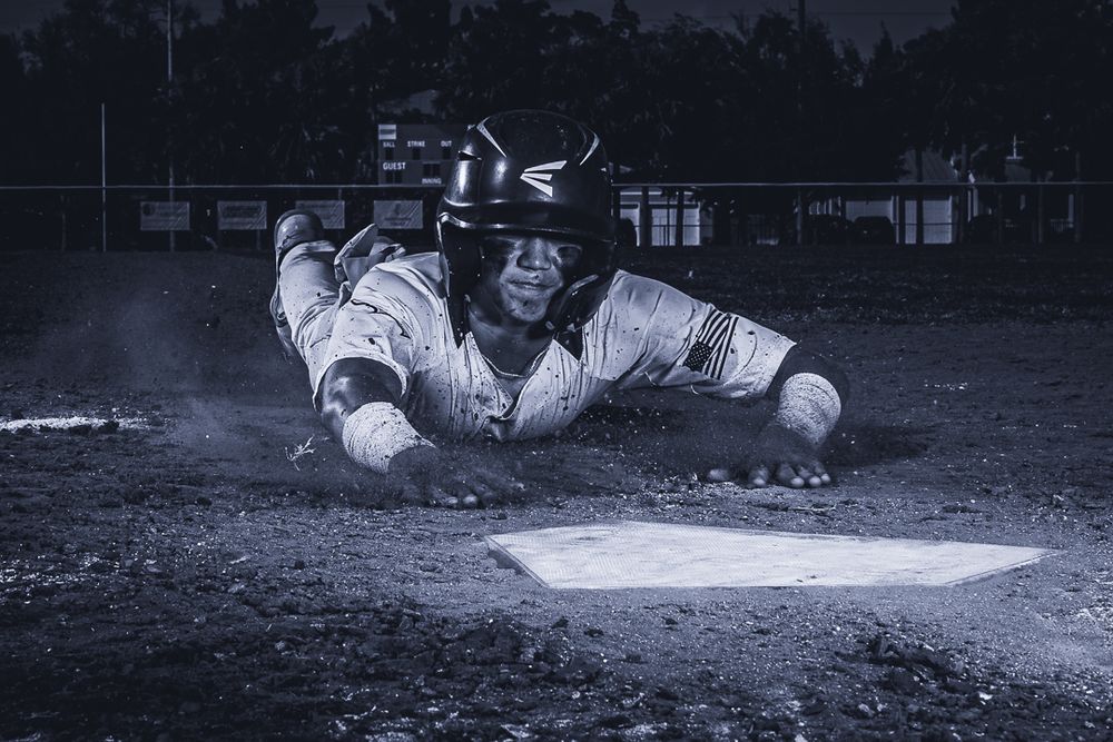 Baseball player slides dramatically into base during game in black and white action shot.