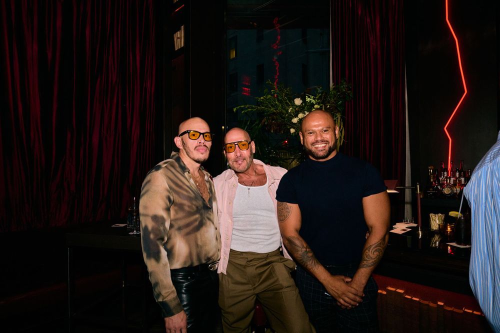 Three friends pose together in front of red curtains at a nighttime venue.
