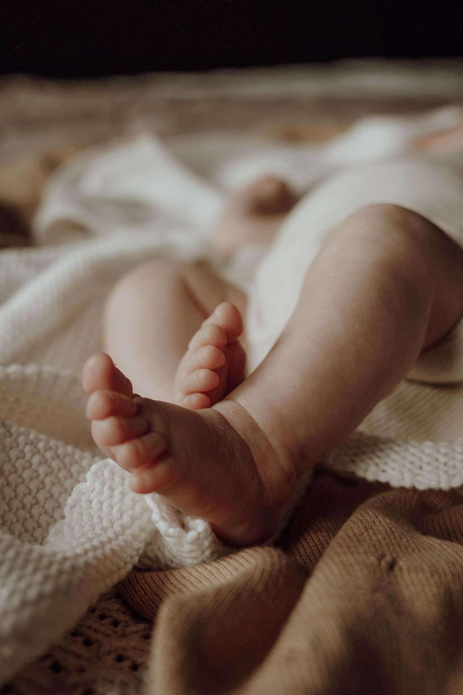 Baby ligt op bed, er is gefocust op de babyvoetjes.