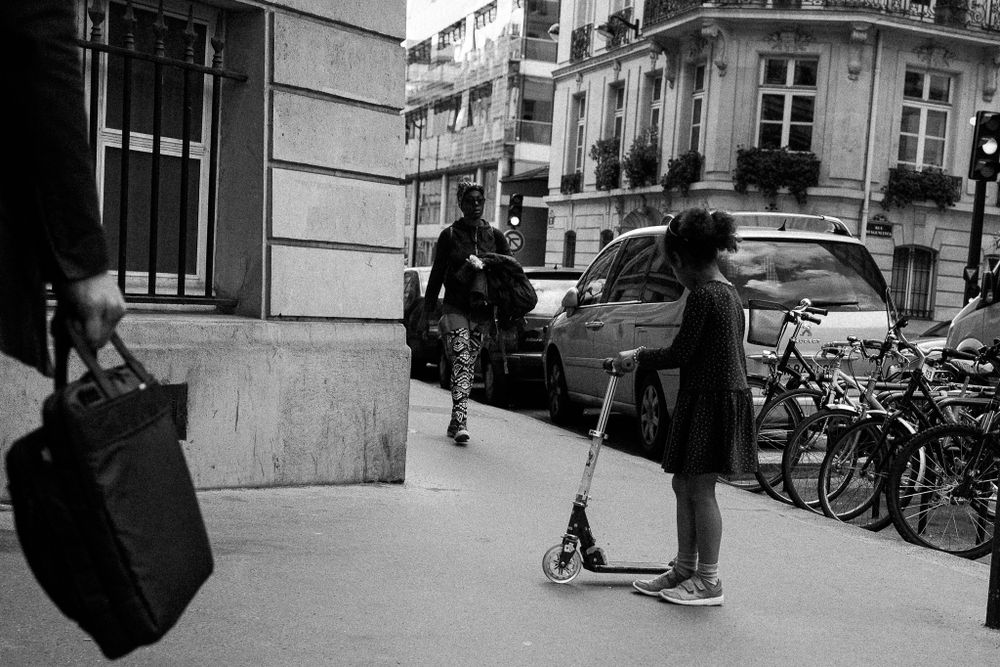 Street scene with scooter riders and parked bicycles in black and white photography.