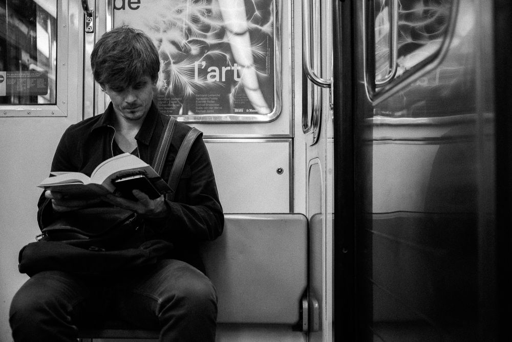 Black and white photo of someone reading a book while riding the subway train.