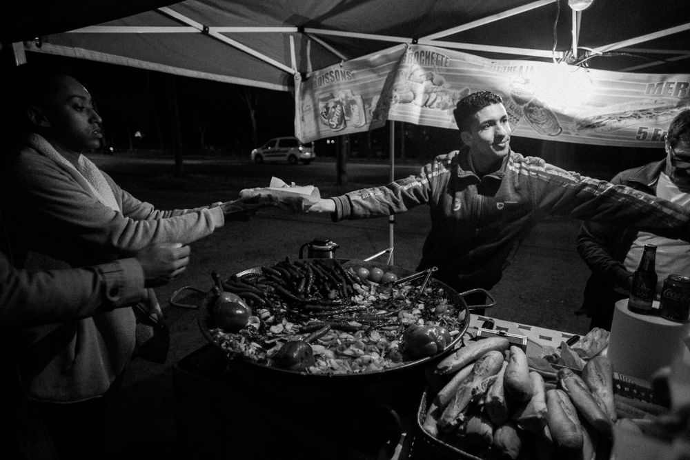 Street vendors working at a food stall at night in black and white.