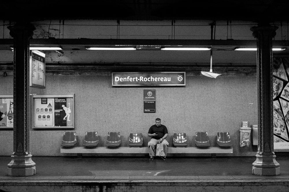 Empty subway platform with lone passenger waiting on bench.