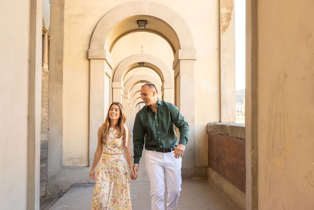 A couple walks through an arched Italian corridor with warm lighting.