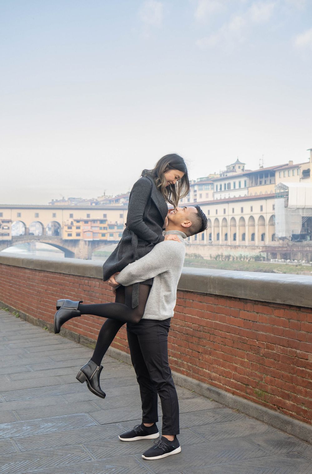 A playful couple shares a romantic moment along the Arno River in Florence.