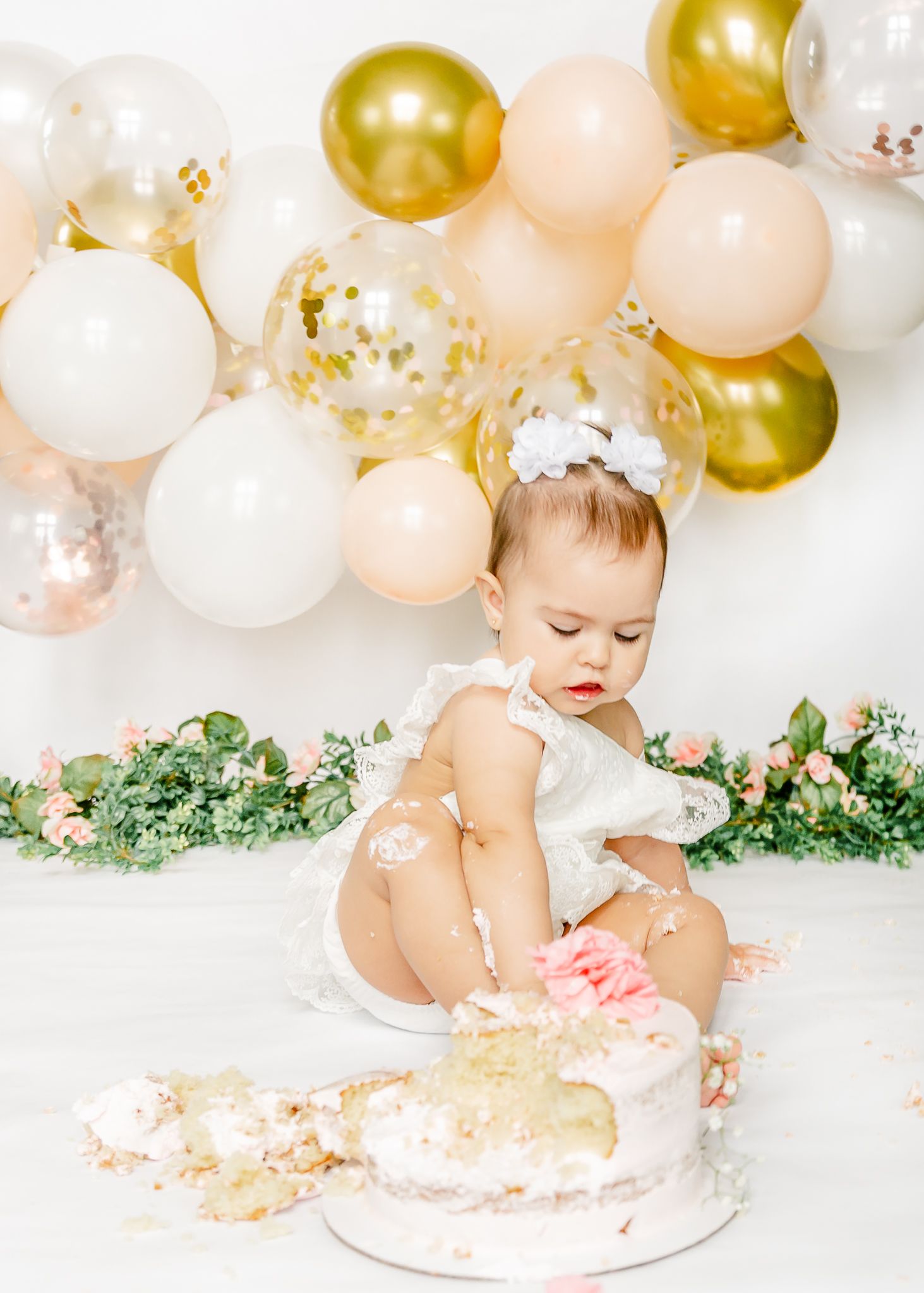 baby girl at her cakesmash photoshoot. with gold ballons garland and classic look.
