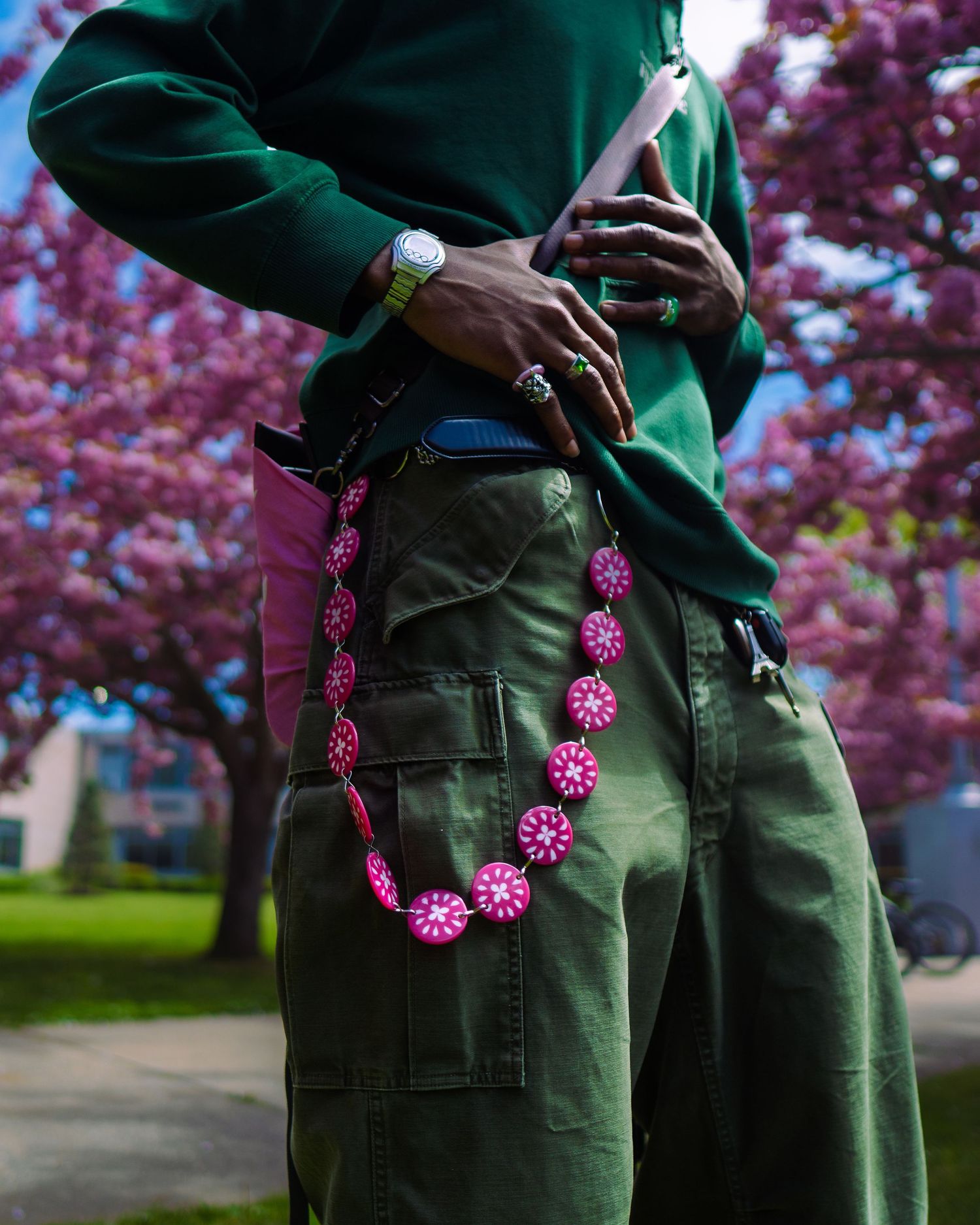 Pink beaded chain and green cargo pants detail against cherry blossom background.