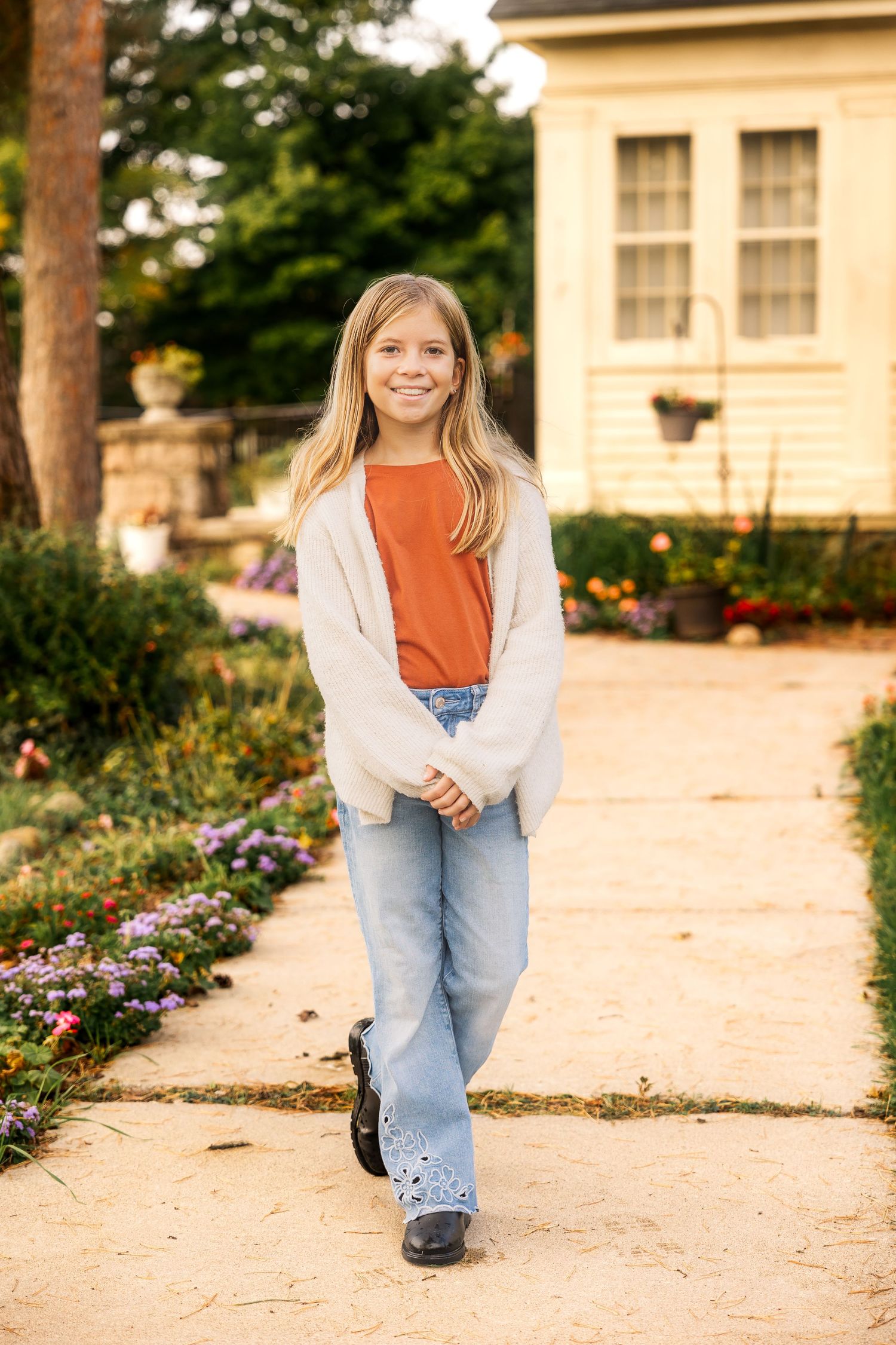 Portrait on garden path wearing orange shirt and cream cardigan against house backdrop. Novi Northville Portrait Photographer