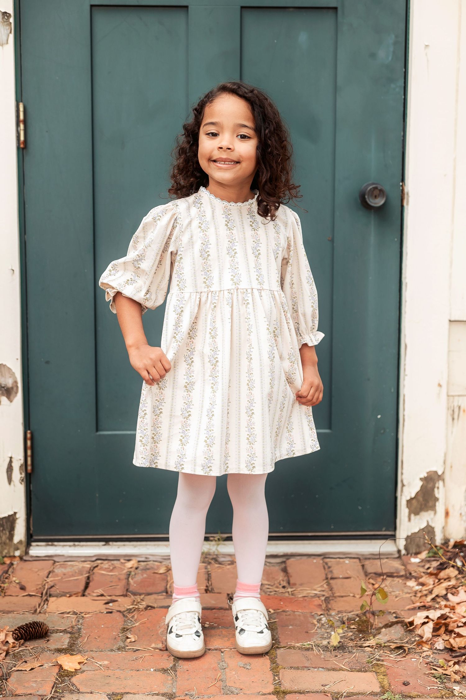 A child in a white eyelet dress poses in front of a green door. Michigan Detroit Novi Northville Portrait Photographer