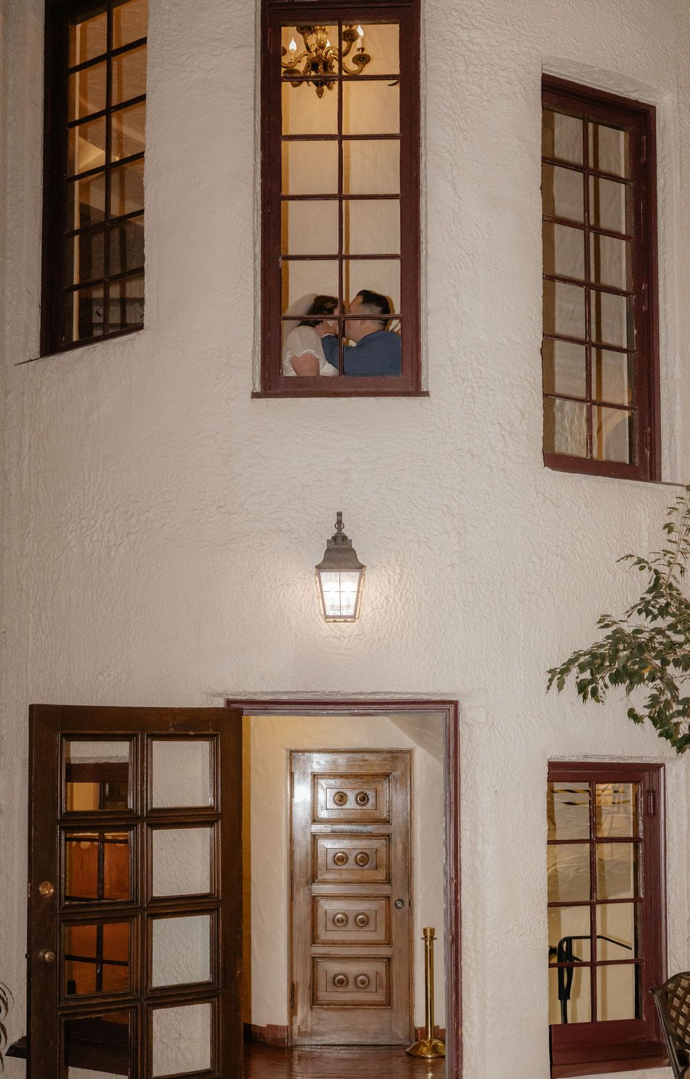 Bride and groom sharing a kiss visible through upper window of elegant white building entrance.