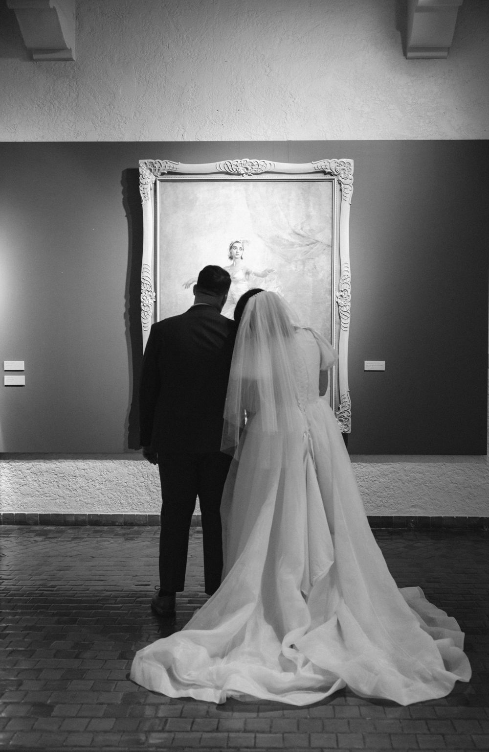 Black and white photo of bride and groom viewing a large portrait painting in a museum.