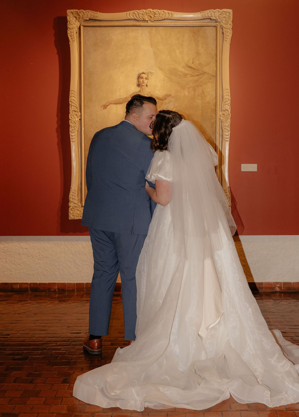 Bride and groom share a romantic moment viewing a framed portrait painting at their wedding venue.