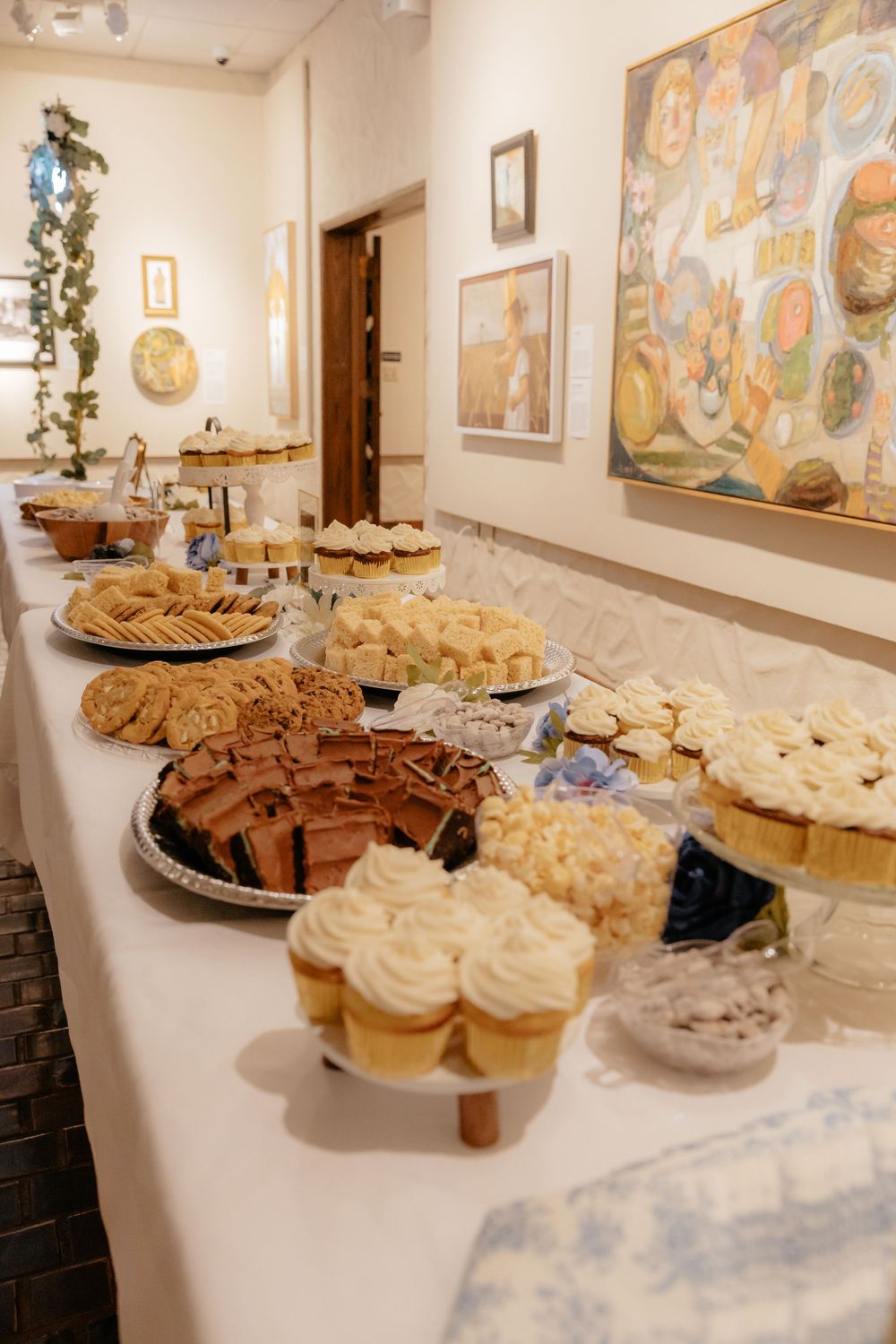 Elegant wedding dessert table featuring cupcakes, cookies, and chocolate treats in an art gallery.