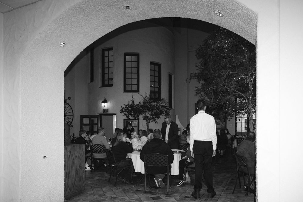 Black and white photo of wedding reception guests seated in an elegant arched venue dining room.